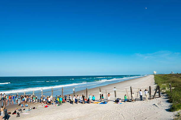 Watching a rocket launch at Cape Canaveral Titusville, Florida, USA - May 15, 2013: Spectators stand along a barrier separating Playalinda Beach from Cape Canaveral and the Kennedy Space Center. They are watching the launch of an Atlas V rocket, which is carrying the U.S. Air Force's fourth Block 2F navigation satellite for the Global Positioning System. The rocket is in the sky, and a plume of smoke on the launch pad. florida beaches map stock pictures, royalty-free photos & images