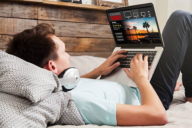 Watching tv series at home. Man watching streaming series in a laptop computer, lying in the bed. spectator stock pictures, royalty-free photos & images