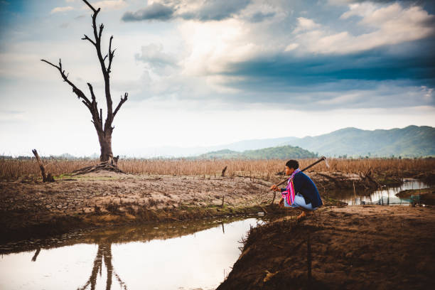 Water crisis concept, Hopeless and lonely farmer sit on cracked earth near drying water. stock photo