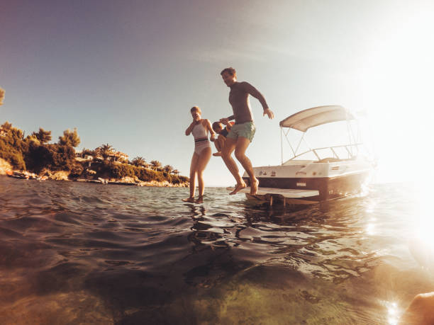 Water jumping with my family Photo of a playful young family jumping off the motorboat and bathing in the sea, during their summer vacation motorboat stock pictures, royalty-free photos & images