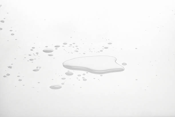 Water puddles and droplets on white reflective surface. Frontal view and deep focus. Frontal view of water spilled on white surface. spilling stock pictures, royalty-free photos & images
