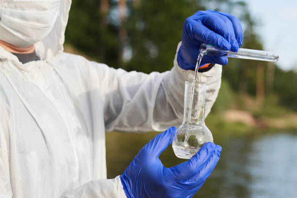 Water Purity Test. Hand in protective gloves holding a chemical flask or test tube with water. Lake in the background. Water Purity Test. Hand holding a chemical flask or test tube with water. Lake or river in the background. water pollution stock pictures, royalty-free photos & images