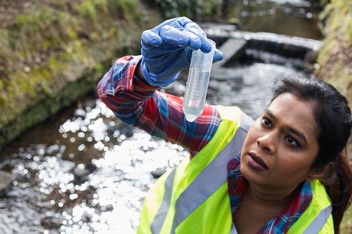A high angle view of a female scientist checking the sample of water in the test tube and seeing if there are any signs of microplastics or pollutants in the water sample she has just collected.