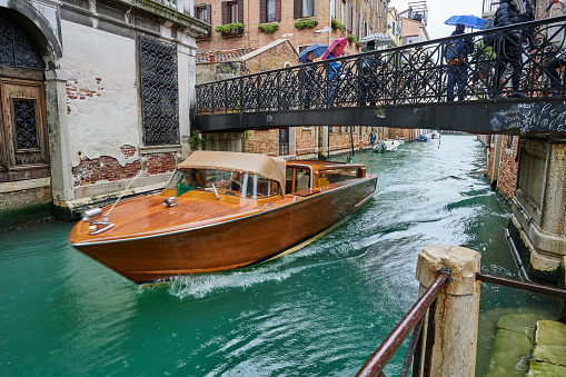 Venice, Italy - November 24, 2019: a water taxi transporting tourists sailing under Bridge De La Bergama in S. Croce Quarter.