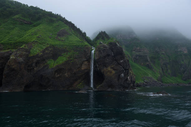 Waterfall dropping from high rocky cliffs into the ocean (Sea of Okhotsk) around the Shiretoko Peninsula stock photo