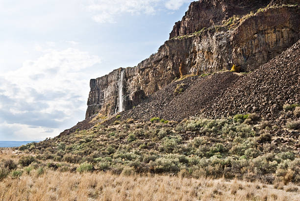 Waterfall Flowing Over a Basalt Cliff East of the Cascade Mountains, Washington’s climate is arid and the terrain is desert-like. Summertime temperatures can exceed 100 degrees Fahrenheit in regions such as the Yakima Valley and the Columbia River Plateau. This is an area of rolling hills and flatlands. During the last Ice Age, 18,000 to 13,000 years ago, floods flowed across this land, causing massive erosion and leaving carved basalt canyons, waterfalls and coulees known as the Channeled Scablands. The Quincy Lakes area is part of the scablands of central Washington State. Visitors to this area will experience basalt cliffs, mesas, benches, canyons and potholes. Several of the potholes have become lakes that are filled with water seeping from the irrigation of nearby upslope farmlands. Ancient and Dusty lakes are two examples that have added to fish and wildlife diversity and have also become important recreational areas. Ancient Lake and Dusty Lake are in the Quincy Wildlife Recreation Area near Quincy, Washington State, USA. jeff goulden waterfall stock pictures, royalty-free photos & images