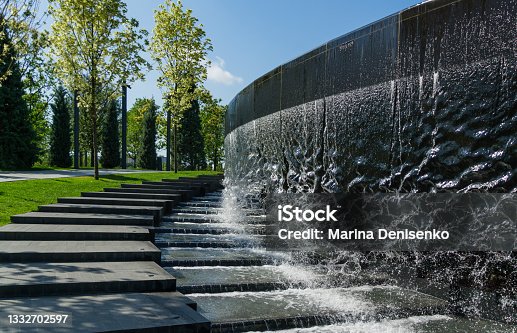 istock Waterfall flows in streams into granite bed of artificial river. Fountain 'Infinity' in form of huge bowl. Public landscape park 'Krasnodar' or 'Galitsky park'. 1332702597