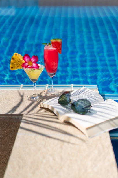 Watermelon and pineapple cocktails, book and sunglasses by the pool with coconut plam tree shadow stock photo
