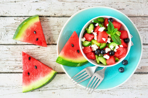 watermeloen salade met komkommer, bosbessen en kaas, top view scene op wit hout - watermeloen stockfoto's en -beelden