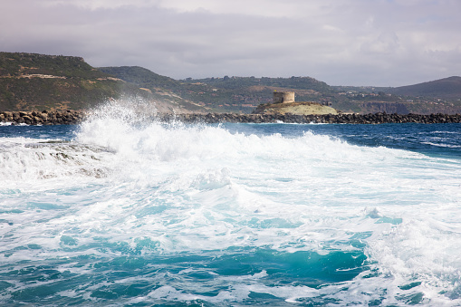 View of waves breaking along the coast with a ruined tower in background, Sardinia, Italy.
