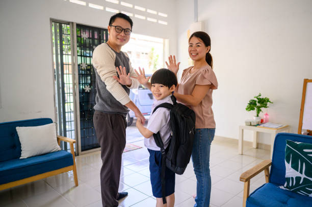 Waving hand before leaving for his first day of school An Asian parent and their son waving hand before leaving on their way out of the front door for his first day at school. wave goodbye asian stock pictures, royalty-free photos & images