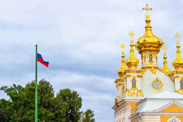 размахивая российским флагом и золотыми куполами храма петра и павла в большом петергофском дворце на фоне облачного неба - vera pauw стоковые фото и изображения