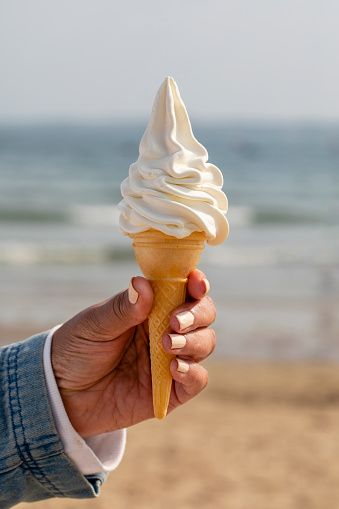 An unrecognisable woman holding an ice cream cone in her hand on Beadnell beach, North East England.