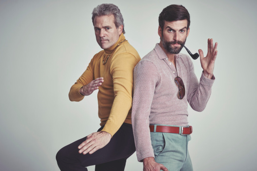 Studio shot of two men standing together while wearing retro 70s wear and striking a fighting pose