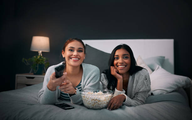 We have everything we need right here Shot of two young women eating popcorn while watching a movie at home asian family eating together stock pictures, royalty-free photos & images