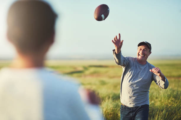 We have so much fun even when just tossing a ball Shot of father throwing a football to his son on a field throwing stock pictures, royalty-free photos & images
