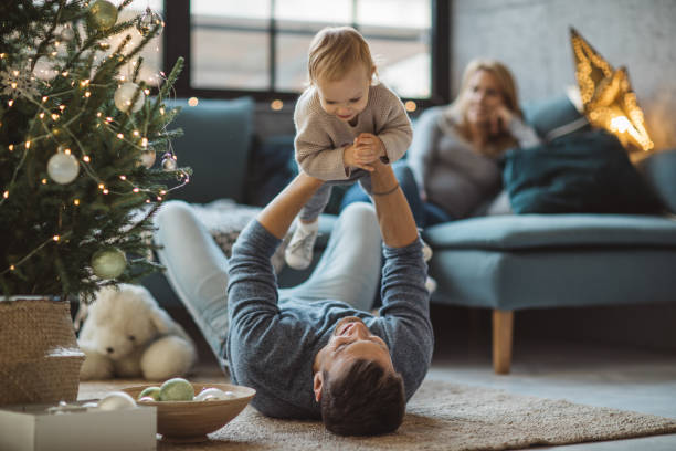 We love to play together Father and daughter having fun at Christmas decorated living room picking up photos stock pictures, royalty-free photos & images