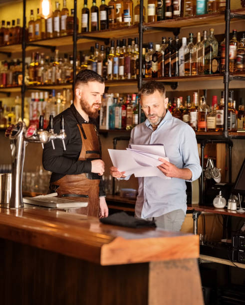 We really need to go over this Shot of a bar manager and bartender checking some documents of the pub bar drink establishment photos stock pictures, royalty-free photos & images