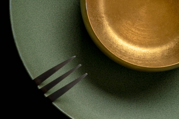 Weathered golden metal bowl and fork on green ceramic plate stock photo