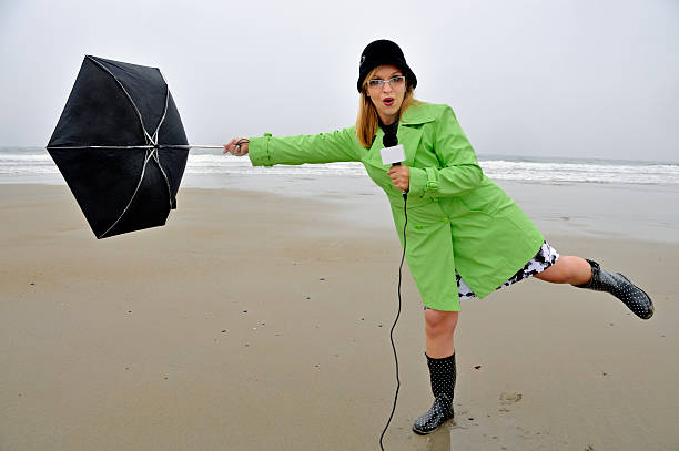 Weathergirl with Umbrella Being Blown Away "Young blonde female reporter/weather girl on location during inclement weather. Series shot at Hampton Beach, NH." mike cherim stock pictures, royalty-free photos & images