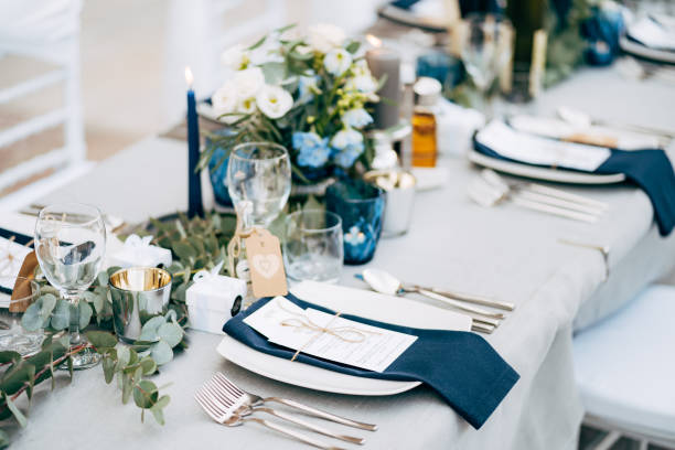 Wedding dinner table reception. A square plate with a blue cloth towel, knives and forks next to the plate. Flower composition with eucalyptus leaves in the center of the table and burning candles. A square plate with a blue cloth towel, knives and forks next to the plate. Flower composition with eucalyptus leaves in the center of the table and burning candles. wedding reception stock pictures, royalty-free photos & images