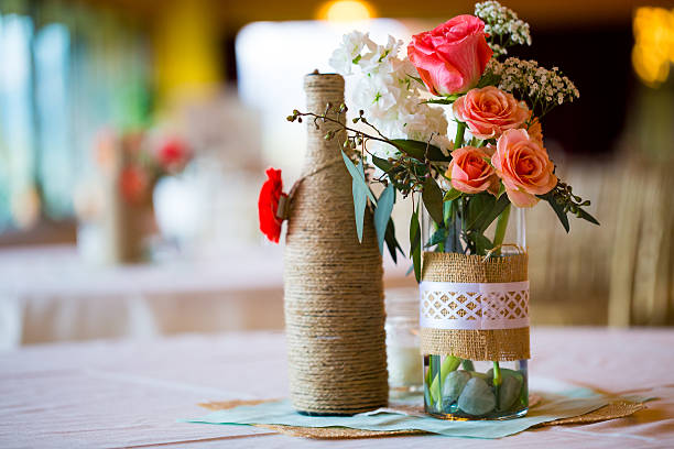 Wedding Reception Table Centerpieces DIY wedding decor table centerpieces with wine bottles wrapped in burlap twine and rose flowers. centerpiece stock pictures, royalty-free photos & images