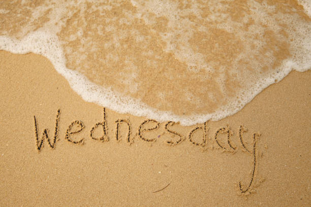 Wednesday - handwritten on the light beach sand with a soft wave lapping. stock photo