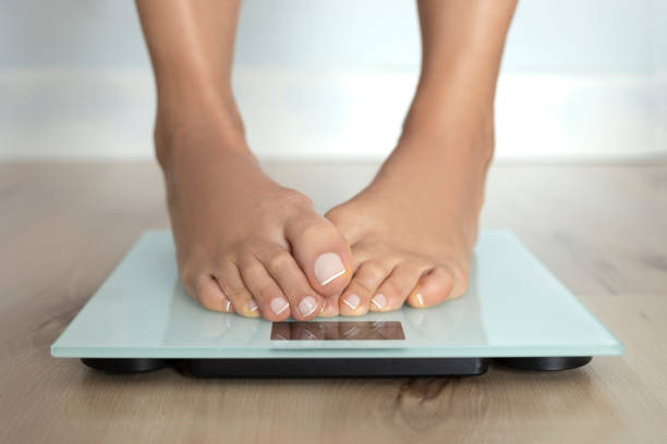 Weighing Scale Ashamed feets of a barefoot female on weighing scale. feet unit of measurement stock pictures, royalty-free photos & images