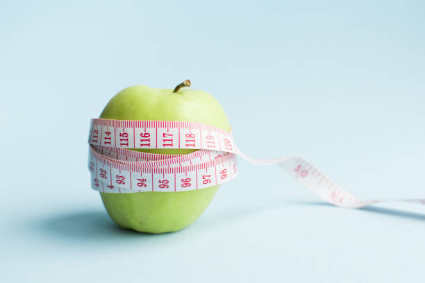 Weight loss and healthy eating concept Apple with measuring tape on blue background. Weight loss, counting calories and healthy eating concept - calculate daily nutrition intake. Copy space. obesity stock pictures, royalty-free photos & images