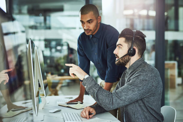 We're always learning in this office Shot of a young businessman assisting a colleague in a call centre it support stock pictures, royalty-free photos & images