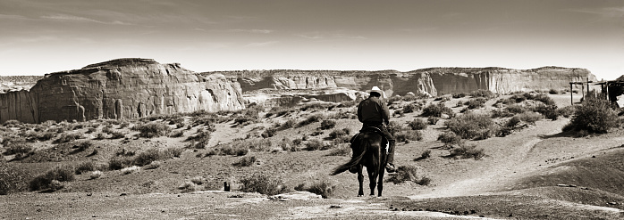 An Native American cowboy on horseback at the Monument Valley Tribal Park in Arizona, USA. A famous tourist destination in the southwest USA. The iconic western landscape is a backdrop for many western movies. The native American is a Navajo tribe native. Photographed on location in black and white