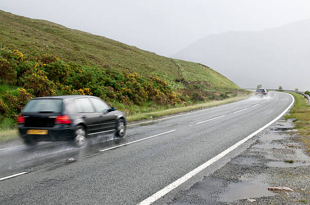 Wet Rural Drive Two cars speed along a winding wet country road in Scotland. hatchback stock pictures, royalty-free photos & images