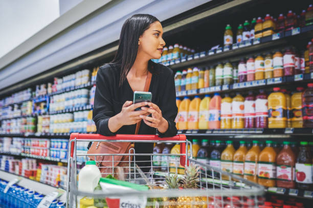 What's a grocery store without wifi Shot of a young woman using a smartphone while shopping in a grocery store chain store stock pictures, royalty-free photos & images