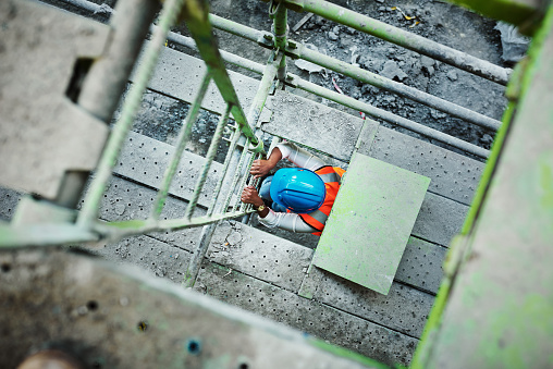 Shot of a young woman climbing up a ladder at a construction site