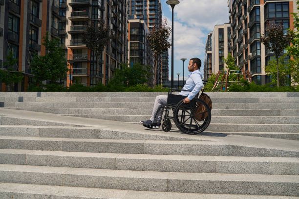 Wheelchair-bound man climbing stairs in business district stock photo