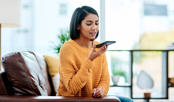 When we're communicating, we're connecting Shot of a young woman using a smartphone on the sofa at home speech recognition stock pictures, royalty-free photos & images