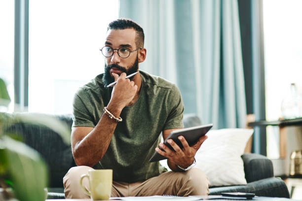 Where's the best place to invest my money? Shot of a young man going over his finances at home contemplation stock pictures, royalty-free photos & images