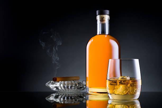 Whiskey glass, bottle and cigar on black glass surface stock photo
