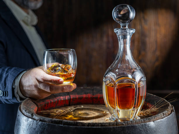 Whisky tasting. Man sits in front of a barrel with a decanter and a glass of whiskey. stock photo