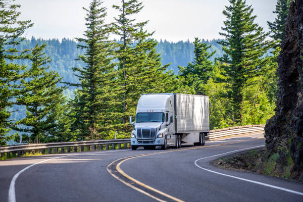 White big rig semi truck transporting goods in refrigerated semi trailer turning on the mountain road with rock wall stock photo