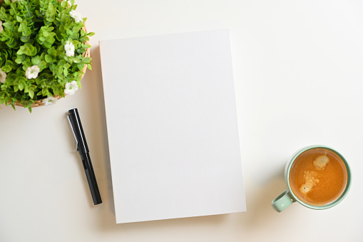 White blank book cover mockup with pen, coffee cup, plant on white background. Top view