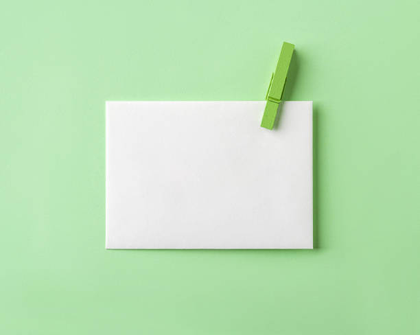 White blank paper with green wooden clothespin against pastel green paper background. Minimalist design template for living green message and greeting card mockup. stock photo