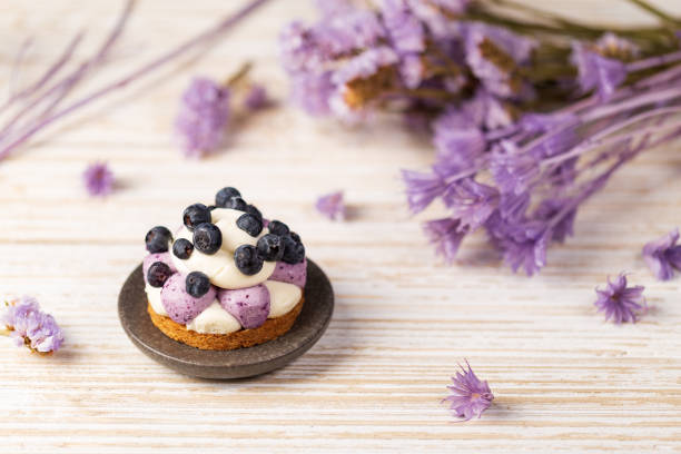 White chocolate and blueberry sable tartelette on a white drift wood table with purple dry flowers background. stock photo