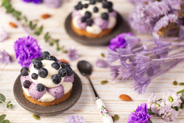 White chocolate and blueberry sable tartelette with vintage spoon on a white drift wood table with purple dry flowers background. stock photo