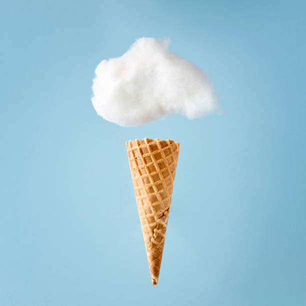 White cloud made of fluffy cotton over an ice cream cone against pastel blue background. stock photo