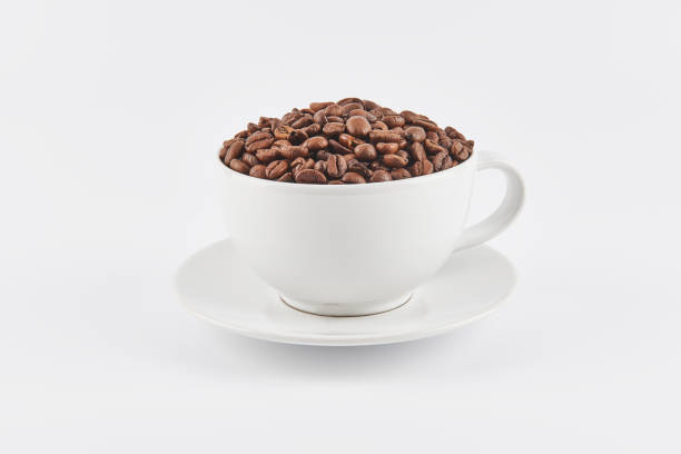 White coffee cup filled with whole coffee beans on a saucer, isolated...
