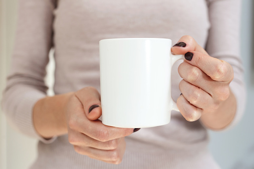 White coffee mug mockup for design demonstration. Stylish cup mock up in female hand.