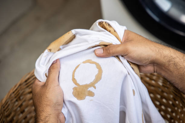 White cotton shirt A lot of stains, stains, coffee stains, man's hand holds the shirt up and spreads it to look dirty Must be brought to the washing machine stock photo