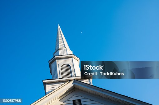istock White Country Church Steeple in the Sunlight with a Blue Sky and Moon 1302517988