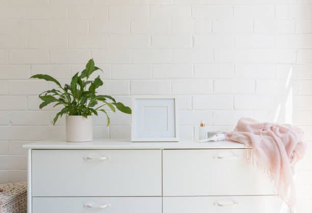 White dresser against wall with pot plant, frame and pink scarf Close up of white dresser against painted brick wall with pot plant, blank square frame, pink scarf and lotions (selective focus) dresser photos stock pictures, royalty-free photos & images